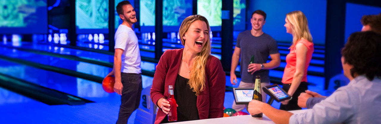 Young adults having a laugh with drinks at the bowling alley